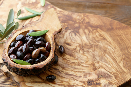 Fresh brown kalamata olives and olive tree leaves in authentic greek wooden bowl with bark, close up viewの写真素材
