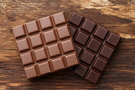 Milk and dark square shape chocolate bars on textured brown wooden background, top viewの写真素材