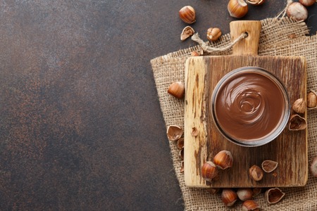 Chocolate spread or nougat cream with hazelnuts in glass jar on brown textured countertop, copy spaceの写真素材