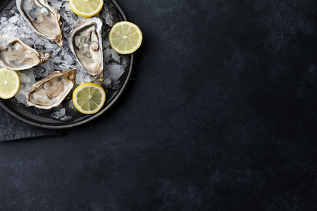 Fresh opened oysters in a plate with ice and lemon on black textured background, top viewの写真素材