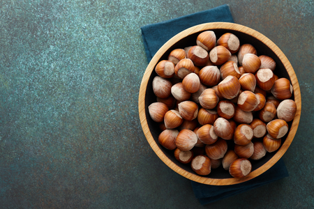 Hazelnuts in a wooden bowl on blue green textured background, copy spaceの写真素材