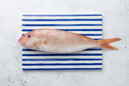 Fresh red mullet fish on striped rectangular plate on white stone background, top viewの写真素材
