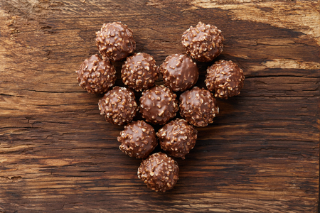 Heart shape made from chocolate truffle candies with hazelnuts on wooden background, top viewの写真素材