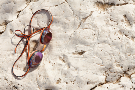 Orange swimming glasses or goggles on cliff rock, close up view. Summer travel concept.の写真素材