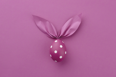 Purple dotted Easter egg with paper bunny ears on purple background. Holiday concept.の写真素材