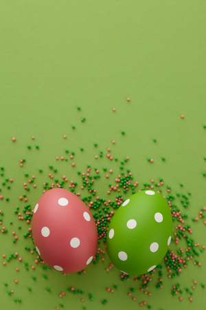 Pair of green and pink dotted Easter eggs on green background, top view. Holiday concept.の写真素材