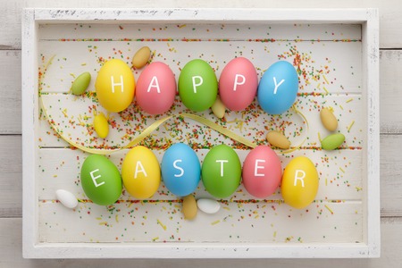Colorful Easter eggs with letters arranged in Happy Easter greeting on white wooden planks. Holiday concept.の写真素材