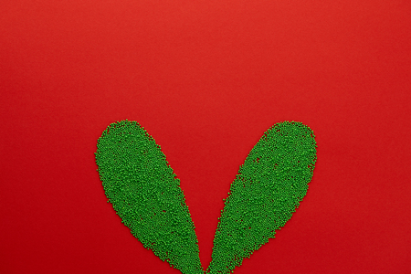 Easter bunny ears shape made from green sugar sprinkles on red background. Holiday concept.の写真素材