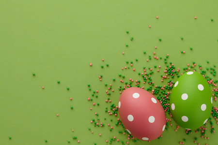Pair of green and pink dotted Easter eggs on green background, top view. Holiday concept.の写真素材
