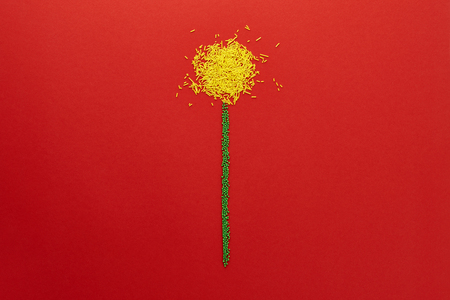 Dandelion flower shape made from Easter sugar sprinkles on red background. Holiday concept.の写真素材