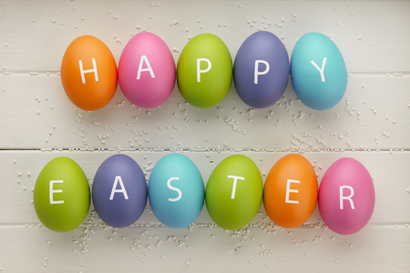 Colorful Easter eggs with letters arranged in Happy Easter greeting on white wooden planks. Holiday concept.の写真素材