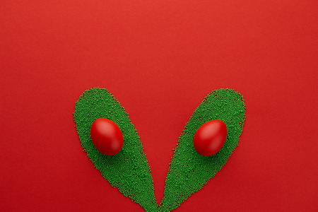 Easter bunny ears shape made from green sugar sprinkles and painted eggs on red background. Holiday concept.の写真素材