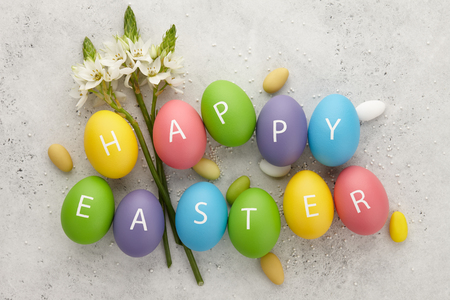 Colorful Easter eggs with letters arranged in Happy Easter greeting and spring flowers on white textured background. Holiday concept.の写真素材
