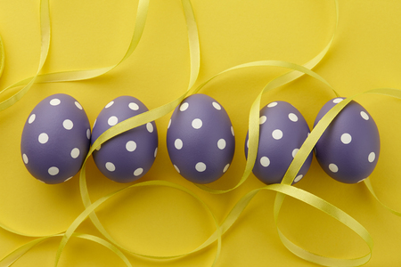 Purple dotted Easter eggs with ribbon on yellow background, top view. Holiday concept.の写真素材