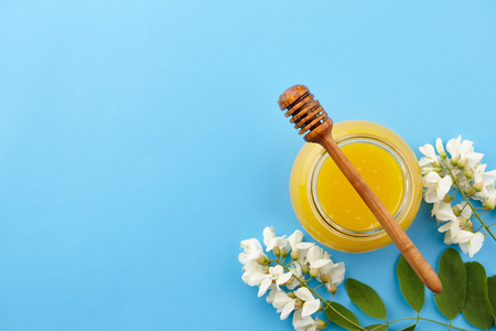 Honey in glass jar and acacia blossoms on blue background, top viewの写真素材