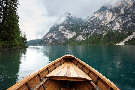Beautiful Lago di Braies and foggy mountains view from wooden boat in rainy weather. South Tyrol, Italy.の写真素材