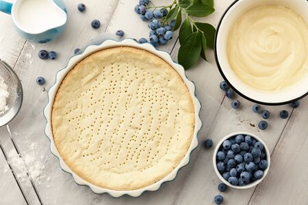 Pie crust, custard and fresh blueberries on white wooden planks. Cooking blueberry pie.の写真素材