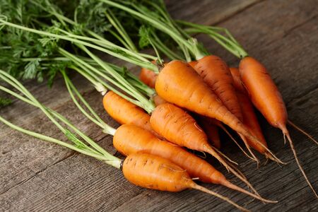 Fresh washed carrots with greens on old wooden planks, close up viewの写真素材