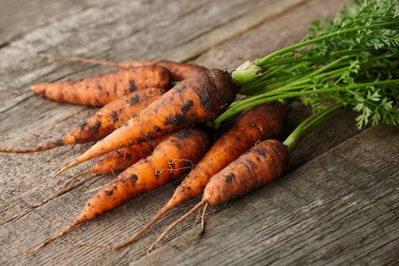Fresh unwashed carrots with greens on old wooden planksの写真素材