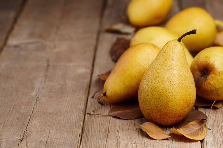 Yellow pears with autumn leaves on wooden table, close up viewの写真素材