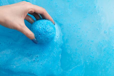 Woman's hand putting blue bath bomb into water, copy spaceの写真素材