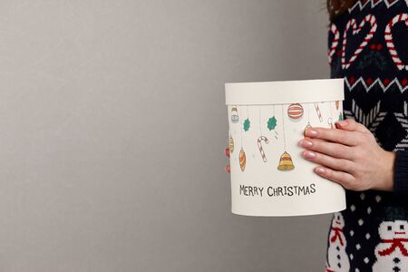 Woman in holiday sweater with Christmas gift box on gray wall background, close up viewの写真素材