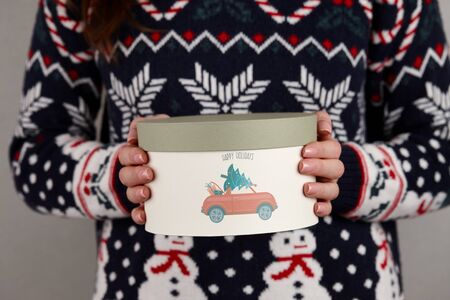 Woman in holiday sweater with Christmas gift box on gray wall background, close up viewの写真素材