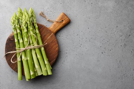 Bunch of fresh green asparagus on wooden cutting board on gray concrete background, top viewの写真素材