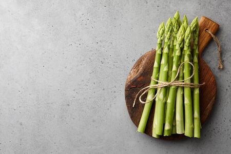 Bunch of fresh green asparagus on wooden cutting board on gray concrete background, top viewの写真素材