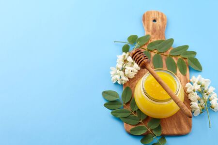 Honey in glass jar and acacia blossoms on blue background, copy spaceの写真素材