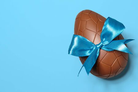 Chocolate Easter egg with blue ribbon bow on blue background, close up viewの写真素材