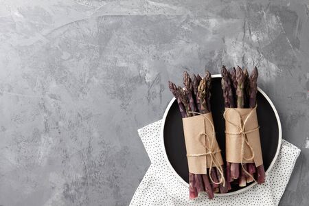 Fresh purple asparagus in black plate on textured stone background, top viewの写真素材