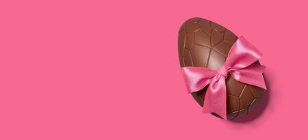 Chocolate Easter egg with pink ribbon bow on pink background, copy spaceの写真素材