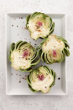 Green artichoke halves with spices in white plate, cooking processの写真素材