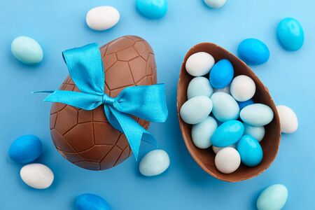 Chocolate Easter egg with colorful candies on blue background, holiday concept