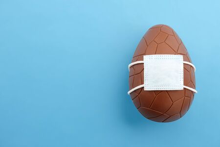 Chocolate Easter egg with corona virus mask, creative holiday concept