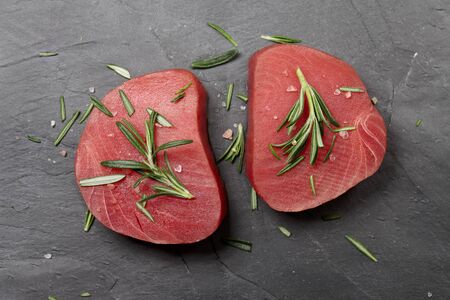 Fresh raw tuna steak with rosemary on black stone background, top viewの写真素材
