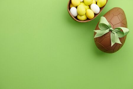 Chocolate Easter egg present with colorful candies on green background, copy spaceの写真素材