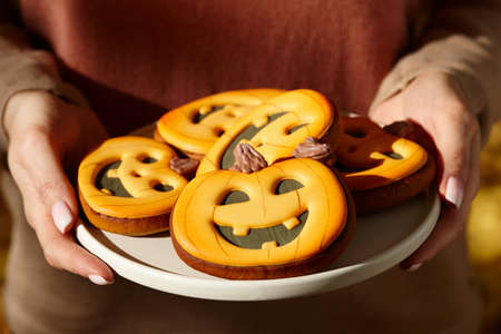 Woman holding halloween gingerbread pumpkins in plate, holiday sweets