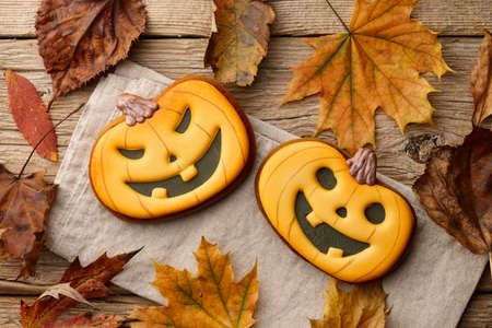 Halloween gingerbread pumpkins on wooden table with autumn leavesの写真素材