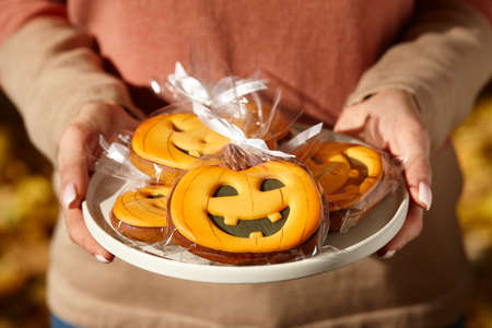 Woman holding halloween gingerbread pumpkins in plate, holiday sweetsの写真素材