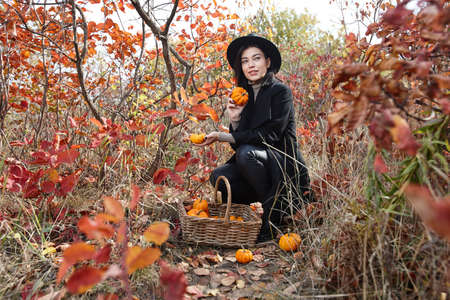 Woman in black with Halloween pumpkins in autumn forest, witch character
