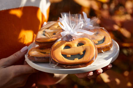 Woman holding halloween gingerbread pumpkins in plate, holiday sweetsの写真素材