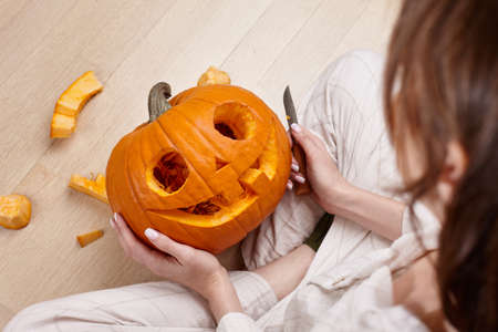 Woman cutting scary pumpkin jack for Halloween, holiday preparationの写真素材