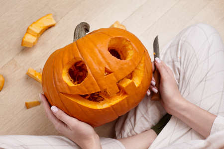 Woman cutting scary pumpkin jack for Halloween, holiday preparationの写真素材
