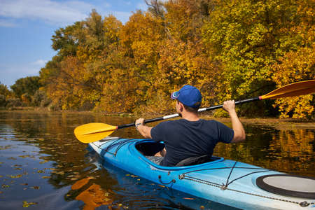 Man kayaking on lake in autumn. Active tourism.