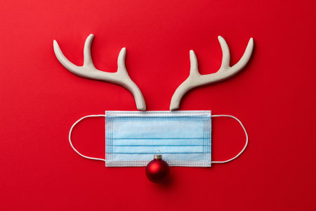 Christmas reindeer made from face mask, antlers and decorations on red backgroundの写真素材