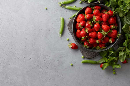 Fresh strawberries, green peas and herbs on concrete table. Seasonal summer food.の写真素材