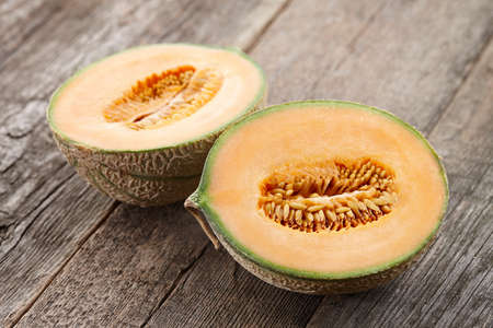 Halves of cantaloupe melon on old wooden planks, close up viewの写真素材
