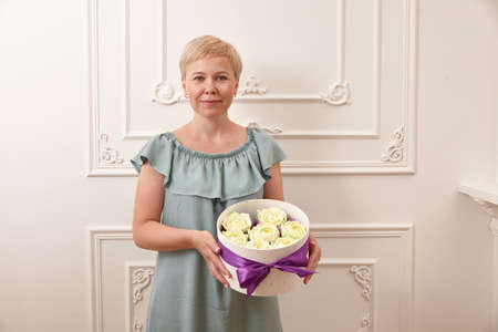 Woman confectioner holding box with flower shaped sweets on white wall backgroundの写真素材